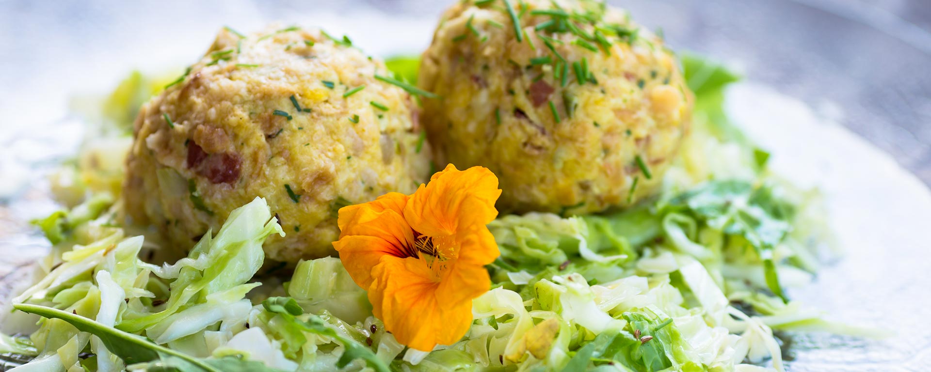 Un gustoso piatto di canederli allo speck, un tipico piatto della cucina ladina, con letto d'insalata di cavolo capuccio e grazioso fiore giallo