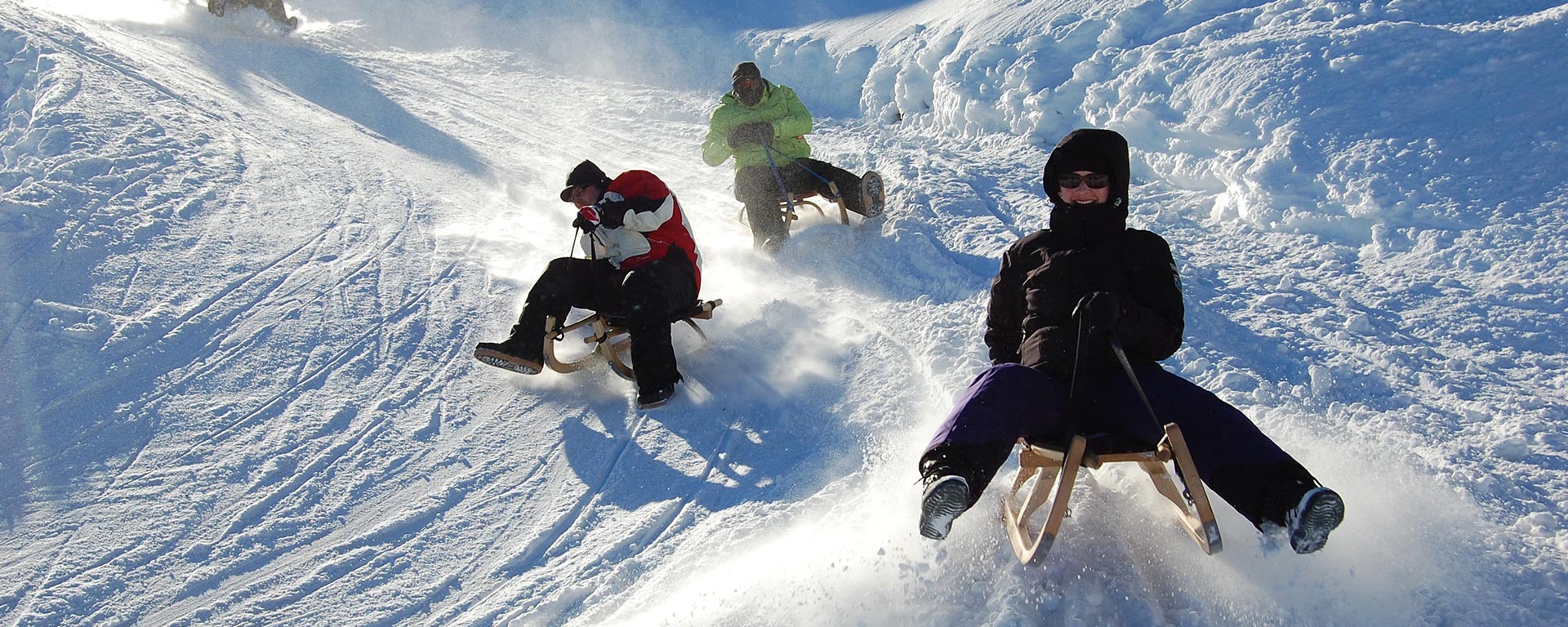a family is having fun on their sleds on a slope in South Tyrol