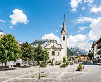 La chiesa parrocchiale e la piazza di San Vigilio di Marebbe con le Dolomiti sullo sfondo