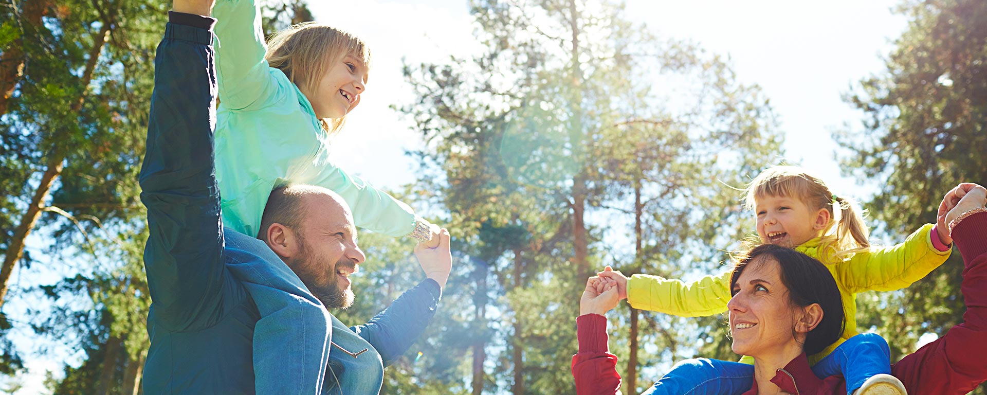 two parents with their daughters on their shoulders during a sunny day in a forest in South Tyrol