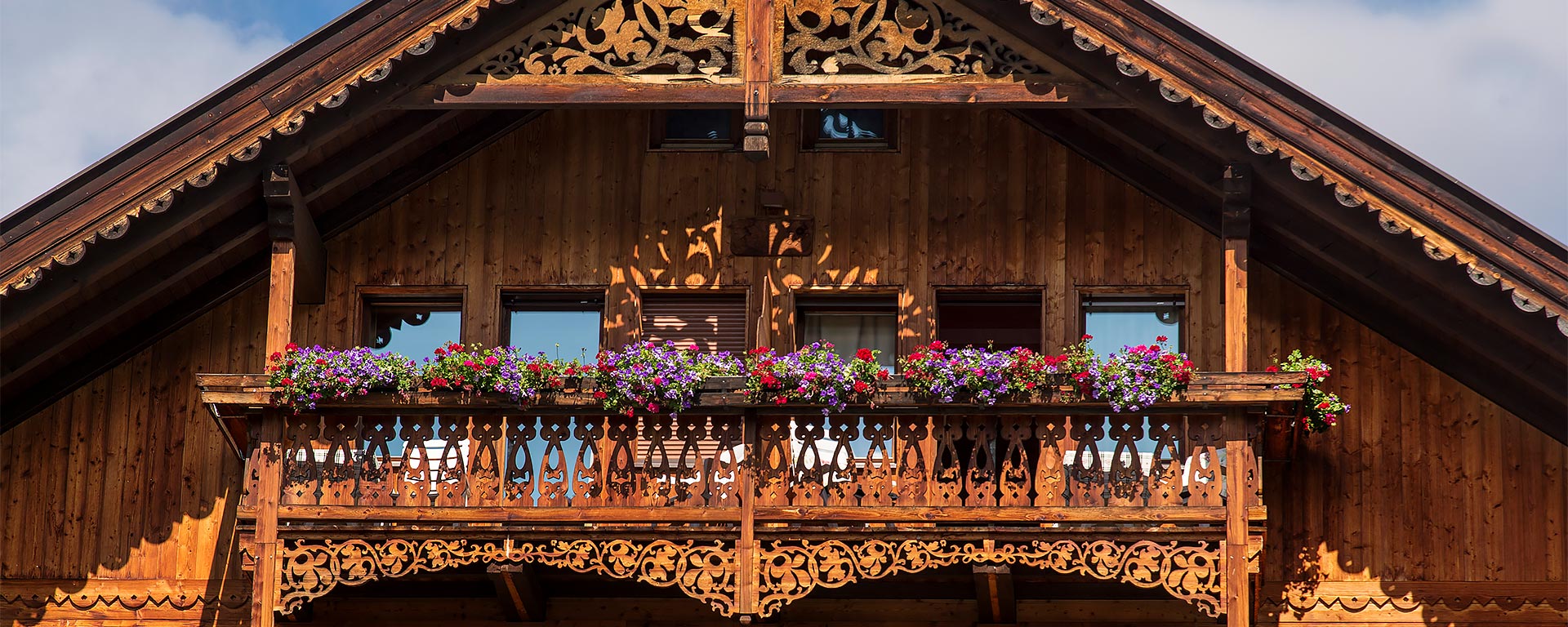 Facciata di un elegante hotel di San Vigilio di Marebbe costruito in legno con spazioso balcone e portafiori